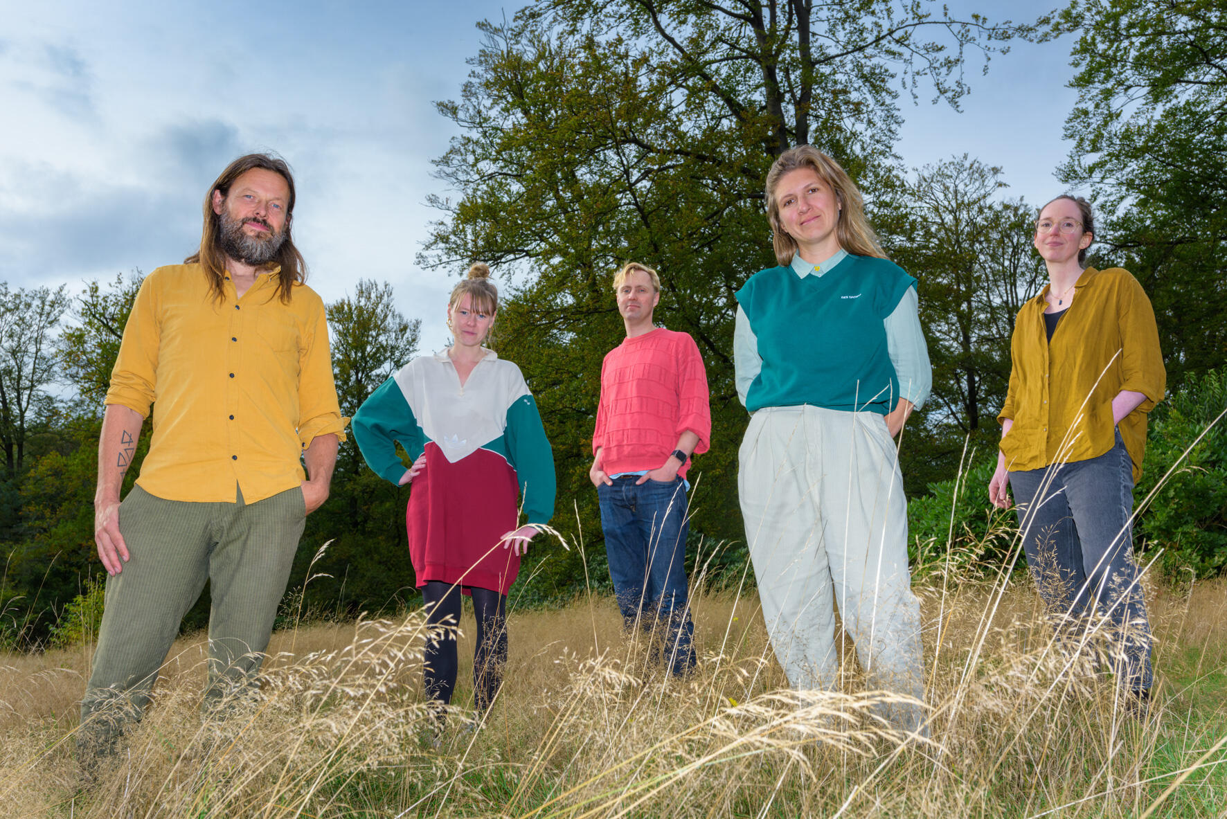 Foto van Floris van Bergeijk die op een bankje zit. Hij heeft donker kort haar en draagt een blauw vest met een rood shirt er onder. Hij zit op een bankje buiten
