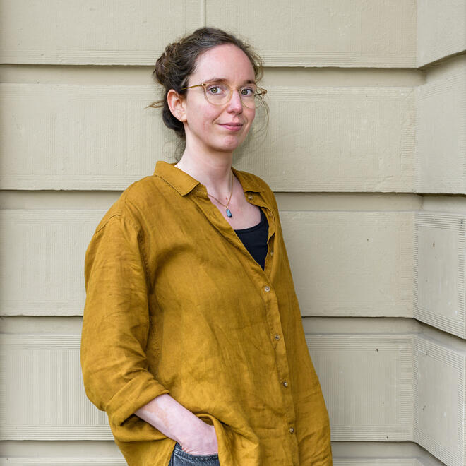 Foto van Marieke van de Ven, een vrouw met donker lang haar. Ze heeft een blauwe trui aan met daaronder een geel shirt en kijkt in de verte.